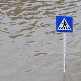 Ein Verkehrszeichen "Fussgängerübergang" ragt auf einer überschwemmten Strasse aus den Fluten hervor. (Foto: picture-alliance / Romain Fellens | Romain Fellens)
