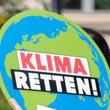 Eine Frau trägt eine Schild in Form der Weltkugel, mit der Aufschrift "Klima retten!" (Foto: picture alliance/Sebastian Willnow/dpa-Zentralbild/dpa)