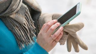 Eine junge Frau schaut auf ihr Handy. Ihre Hanschuhe hält sie mit einer Hand fest (Foto: picture alliance / dpa Themendienst | Christin Klose)