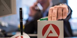 Ein Mann sitzt in der Bundesagentur für Arbeit. Notizblock und Stifthalter mit Logo der Agentur auf dem Schreibtisch. (Foto: picture alliance/dpa | Ole Spata)