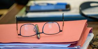 Eine Brille liegt auf einer Aktenmappe mit einigen Unterlagen (Foto: picture alliance/dpa/dpa-Pool | Axel Heimken)