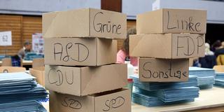 Stimmzettel werden bei einer Wahl ausgezählt, Kartons mit Parteien beschriftet stehen auf einem Tisch (Foto: picture alliance/dpa | Georg Wendt)
