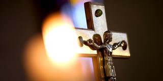 Eine Kerze vor einem Kreuz mit einer Jesusfigur (Foto: dpa)