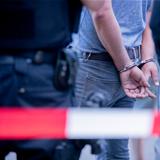 Symbolbild: Eine mit Handschellen gefesselte Person und zwei Polizisten. (Foto: picture alliance/dpa | Christoph Soeder)