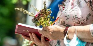 Eine Gottesdienstbesucherin hält ein traditionelles Kräutergebinde und ein Gesangsbuch in den Händen (Foto: picture alliance/dpa | Matthias Balk)