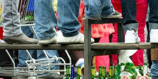 Zuschauer eines Straßenumzugs stehen auf einer Bank unter der sich leere Bierflaschen sammeln (Foto: picture alliance / dpa | Martin Gerten)