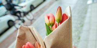 Eine Frau geht mit frischen Tulpen-Sträußen in Papier gewickelt auf der Straße (Foto: picture alliance/dpa | Annette Riedl)