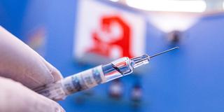 Ein Apotheker hält eine Spritze mit Grippeschutzimpfstoff vor dem Apotheke-Logo. (Foto: picture alliance/dpa | David Inderlied)