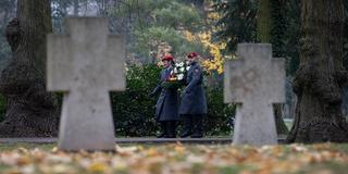 Bundeswehr-Angehörige tragen einen Kranz an einem Gräberfeld für gefallene Soldaten. (Foto: picture alliance/dpa | Ronny Hartmann)
