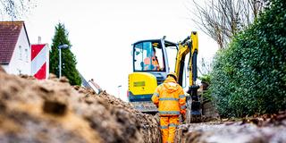 Arbeiter sind mit Bagger und Spaten an einer Straße mit der Erdverlegung von Glasfaserkabeln beschäftigt. (Foto: picture alliance/dpa | Moritz Frankenberg)