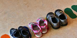 Schuhe stehen in einer  Kita vor einer Spielecke. (Foto: picture alliance/dpa | Bernd Settnik)