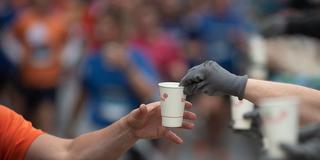 Ein Läufer nimmt während des Firmenlaufs einen Einweg-Becher mit Wasser von einem Helfer entgegen. (Foto: picture alliance/dpa | Sebastian Gollnow)