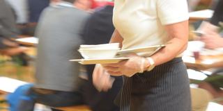 Eine Kellnerin in einem Lokal serviert Essen an Gäste. (Foto: picture alliance / Zoonar | Elmar Gubisch)