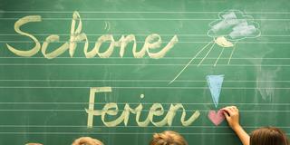 Ferienbeginn. Drittklässler einer Grundschule schreiben "Schöne Ferien!" auf eine Tafel in einem Klassenzimmer. (Foto: picture alliance / dpa | Armin Weigel)
