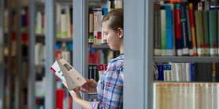 Eine Studentin blättert in einer Hochschulbibliothek in einem Buch. (Foto: picture alliance / dpa | Patrick Pleul)
