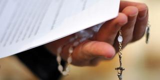 Ein Priester hält einen Rosenkranz und Papier in der Hand (Foto: picture alliance / dpa | Jochen Lübke)