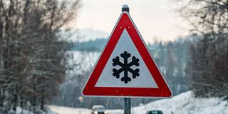 Ein Verkehrsschild mit einer Schneeflocke, das vor glatter Fahrbahn warnt steht am Straßenrand (Foto: picture alliance/dpa | Armin Weigel)