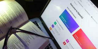 Ein aufgeschlagenes Buch liegt vor einem Bildschirm der OpenAI, bzw. ChatGPT zeigt (Foto: picture alliance/dpa | Karl-Josef Hildenbrand)