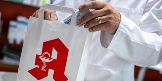 Ein Apotheker legt ein Medikament in eine Papiertasche mit Apotheken-Logo (Foto: picture alliance/dpa | Monika Skolimowska)