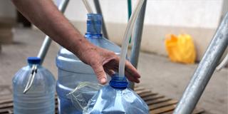 Ein Mann füllt an einer Wasserstelle in mehrere Plastikflaschen Wasser ab. (Foto: picture alliance / AA | Gian Marco Benedetto)