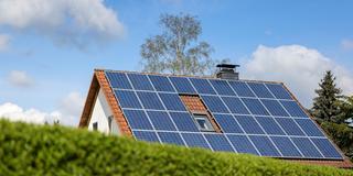 Ein Einfamilienhaus mit Solarpaneelen auf dem Hausdach steht hinter einer grünen Hecke. (Foto: picture alliance/dpa/dpa-Zentralbild | Jan Woitas)