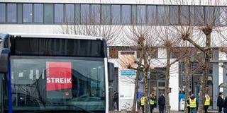 Bus mit Streikplakaten in der Windschutzscheibe und Busfahrer mit gelben Westen im Hintergrund. (Foto: picture alliance/dpa | Laszlo Pinter)