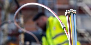 Ein Bauarbeiter steht hinter Leerrohren für Glasfaserkabel, die aus der Erde ragen (Foto: picture alliance/dpa | Sebastian Gollnow)