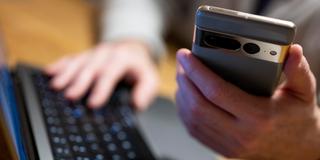 Ein Mann sitzt am Laptop und hält ein Smartphone mit in der Hand. (Foto: picture alliance/dpa | Monika Skolimowska)