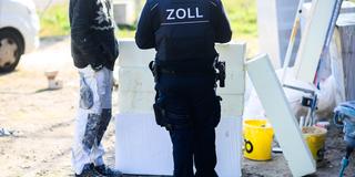 Ein Zollbeamter steht auf einer Baustelle neben einem Bauarbeiter. (Foto: picture alliance/dpa | Julian Stratenschulte)