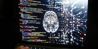 Eine Person arbeitet am Rechner, auf dessen Bildschirm ein durch Künstliche Intelligenz generiertes Illustrationsbild mit Code verschiedener Programmiersprachen und einem neuronalen Netzwerk-Diagramm zu sehen ist (Foto: picture alliance/dpa | Oliver Berg)