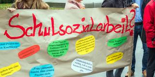 Teilnehmer einer Demonstration halten ein Plakat mit der Aufschrift «Schulsozialarbeit» hoch (Foto: picture alliance/dpa/dpa-Zentralbild | Jens Büttner)