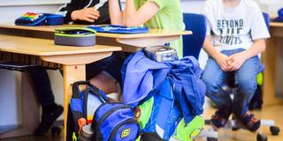 Rucksäcke stehen neben Grundschülern in einer Klasse  (Foto: picture alliance/dpa | Julian Stratenschulte)