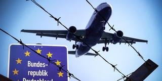 FOTOMONTAGE: Ein Flugzeug fliegt über einen Stacheldrahtzaun.  (Foto: picture alliance / CHROMORANGE | Michael Bihlmayer)