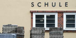 Baumaterialien vor einem Gebäude mit der Aufschrift „Schule“ (Foto: picture alliance/dpa/dpa-Zentralbild | Hendrik Schmidt)