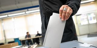 Jemand wirft wirft in einem Wahllokal einen Stimmzettel für die Bundestagswahl in eine Wahlurne (Foto: picture alliance/dpa | Sina Schuldt)