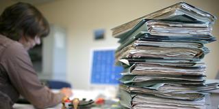 Ein Stapel Akten liegt auf einem Schreibtisch vor einem Computer (Foto: picture alliance/dpa | Patrick Pleul)