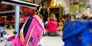 Ein Schulranzen hängt in einer Klasse am Haken eines Schülerpults. (Foto: picture alliance / dpa | Matthias Balk)