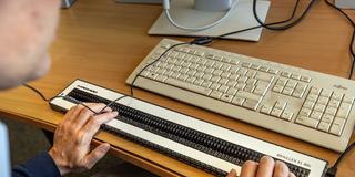 Jemand sitzt an einem Computer-Arbeitspatz mit einer Blindentastatur, die haptisch ertastbare Braille-Schrift ausgibt (Foto: picture alliance/dpa | Dieter Menne)