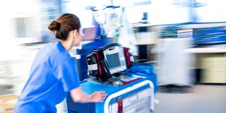 Eine Mitarbeiterin auf der Intensivstation schiebt einen Wagen mit einem Defibrillator zu einem Notfall (Foto: picture alliance/dpa | Sina Schuldt)