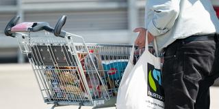 Eine Mann sortiert neben einem gefüllten Einkaufswagen seine Einkäufe in einen Stoffbeutel. (Foto: picture alliance/dpa | Sebastian Kahnert)