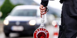 Ein Polizist hält eine Anhaltekelle in der Hand mit einem Auto im Hintergrund (Foto: picture alliance / dpa | Matthias Balk)