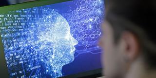 Jemand blickt auf eine symbolische Manifestation einer künstlichen Intelligenz auf einem Computerbildschirm (Foto: picture alliance/dpa | Matthias Bein)