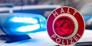 Ein Polizist hält eine Polizeikelle für eine Kontrolle. Im Hintergrund das Blaulicht auf einem Polizeiauto.  (Foto: picture alliance/dpa | Jan Woitas)