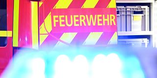 Ein Fahrzeug der Feuerwehr steht bei einem Einsatz auf einer Straße, während im Vordergrund das Blaulicht eines Polizeifahrzeugs zu sehen ist (Foto: picture alliance/dpa | Bernd Weißbrod)