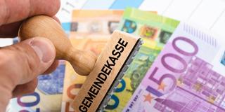 Holzstempel mit der Aufschrift Gemeindekasse über Euro-Banknoten. Symbol für kommunale Einnahmen, Steuern, öffentliche Haushaltsführung. (Foto: picture alliance / CHROMORANGE | Michael Bihlmayer)