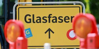 Ein Schild mit der Aufschrift "Glasfaser" steht hinter einer Baustelle. (Foto: picture alliance/dpa | Michael Reichel)