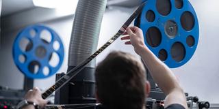 Eine Person hält eine 35mm Filmrolle im Projektor im Kino-Vorfuehrraum (Foto: picture alliance / epd-bild | Tim Wegner)