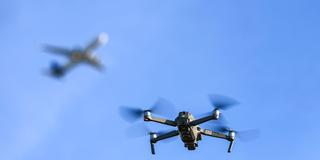 Eine Drohne fliegt am Himmel, im Hintergrund ist ein Flugzeug zu sehen. (Foto: picture alliance/dpa | Jan Woitas)