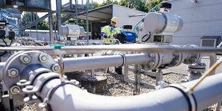 Ein Mitarbeiter der Firma Enovos Storage GmbH steht am 18.07.2022 auf dem Gelände des Gasspeichers Frankenthal hinter Rohren einer Verdichteranlage. (Foto: picture alliance/dpa | Uwe Anspach)