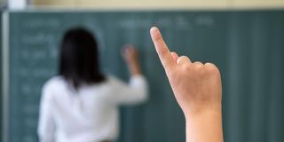 Ein Schüler meldet sich in einer Unterrichtsstunde, während eine Lehrerin an die Tafel schreibt.     (Foto: picture alliance/dpa | Marijan Murat    )
